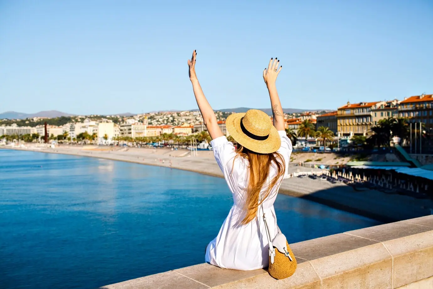 A joyful, elegant woman poses with her back turned, raising her hand in the air and enjoying an amazing view.