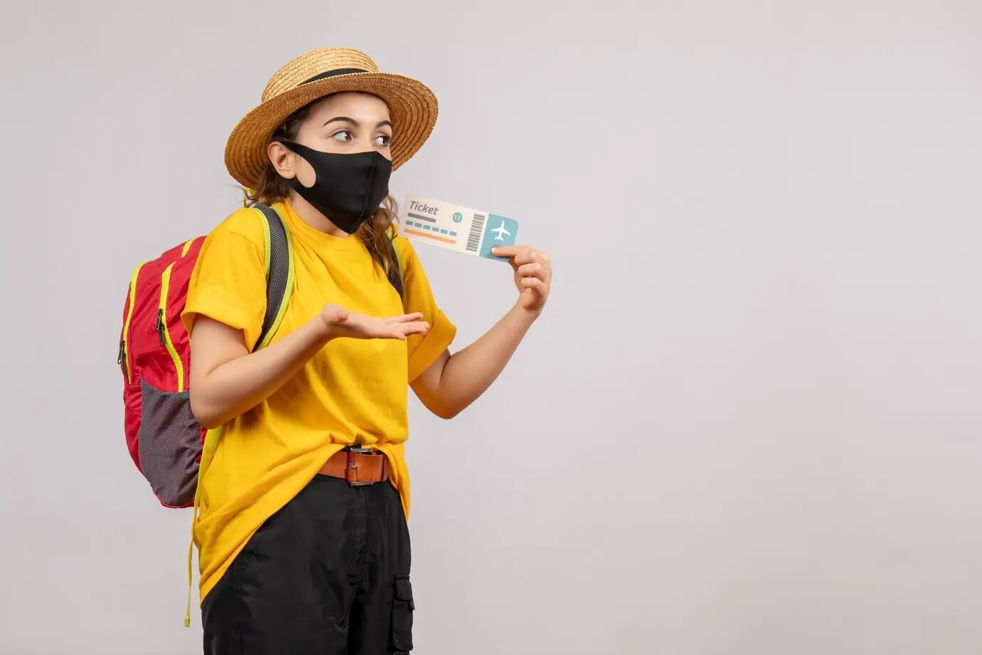 Front view of a young traveller with a red backpack holding up a travel ticket.
