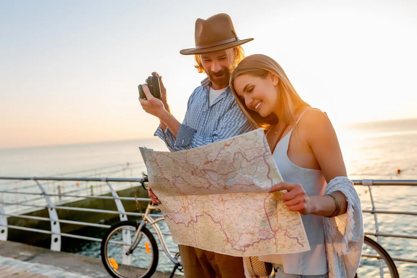 A happy couple traveling by bicycle in summer, looking at a map and taking photos with a camera.